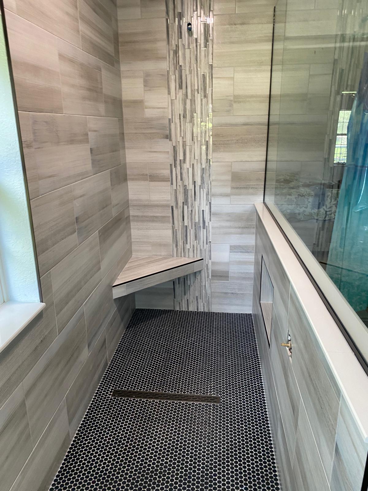 Wood-look plank tile shower with floating bench and black penny-round pan, built in Tampa