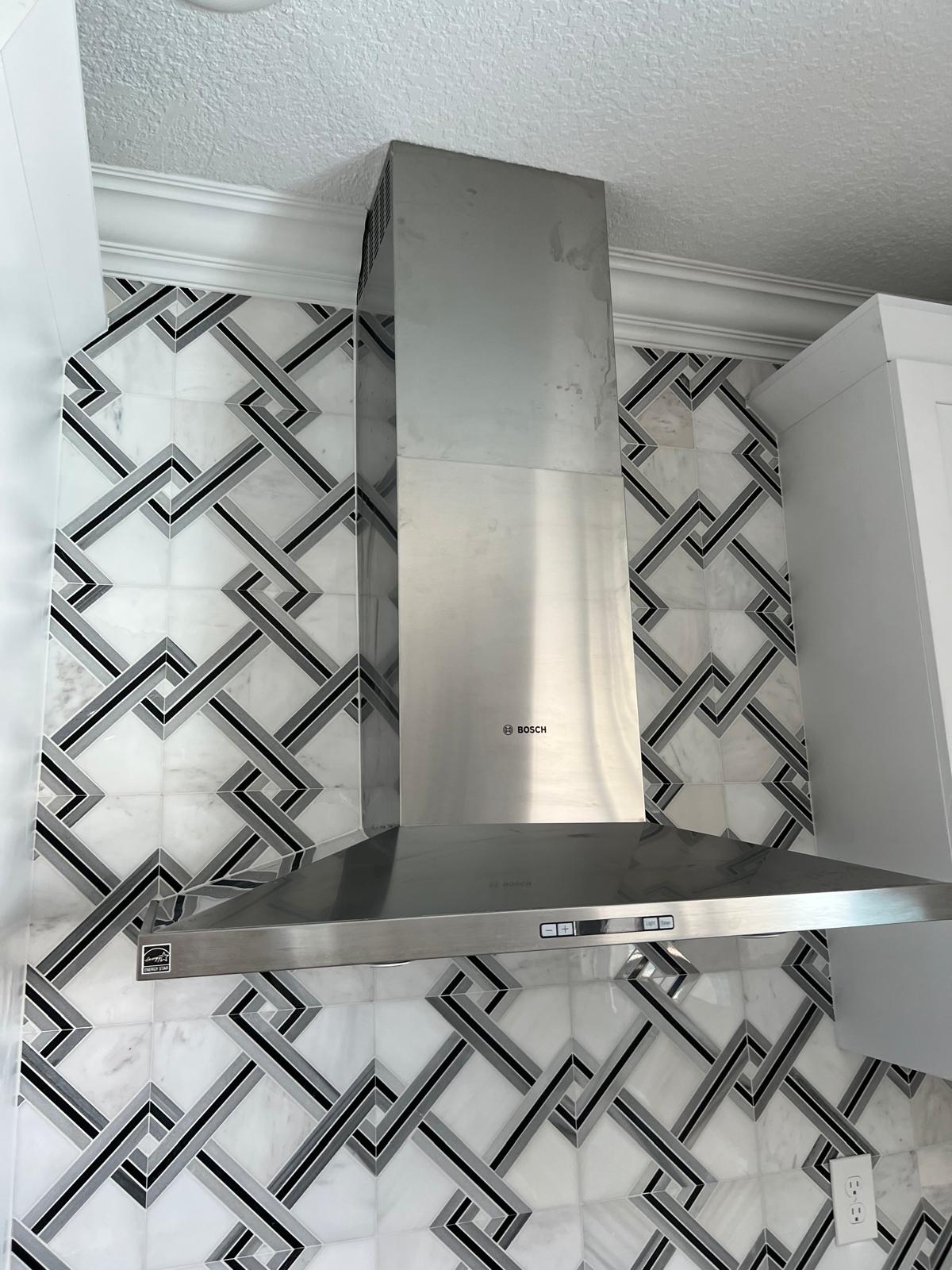 Waterjet marble and brushed metal lattice backsplash behind a stainless range hood