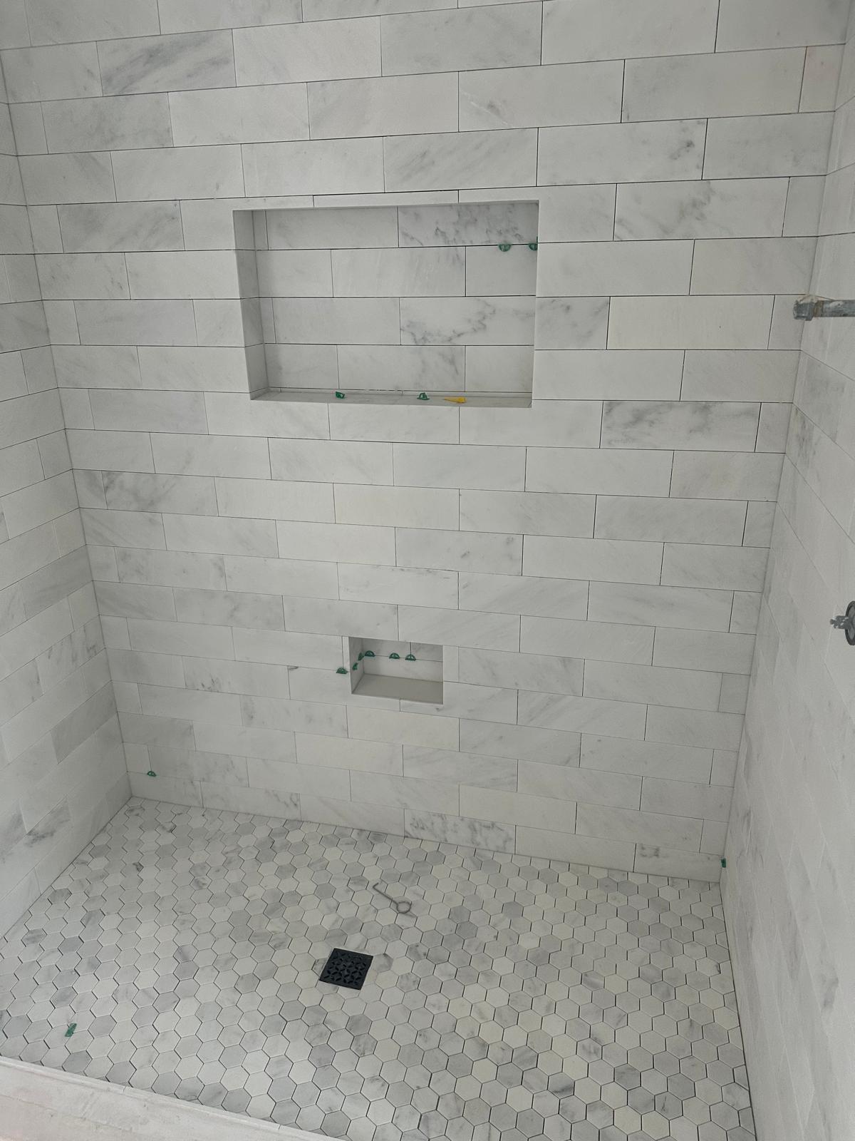 Carrara marble subway tile shower with twin recessed niches and a hex mosaic pan